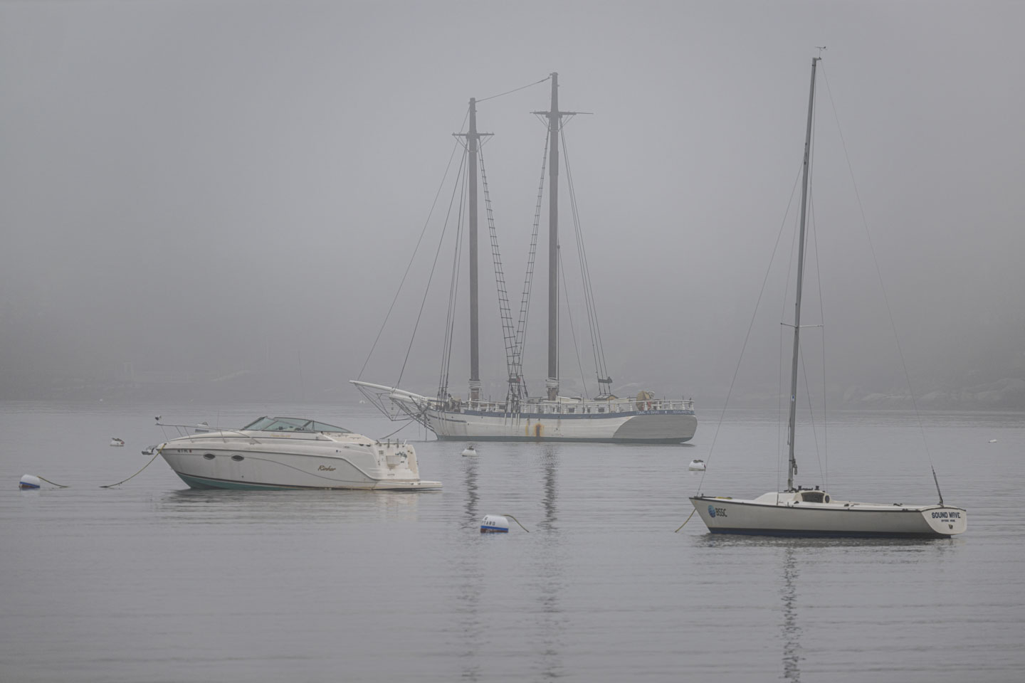 Amid the fog, 3 boats can be seen in the water. 