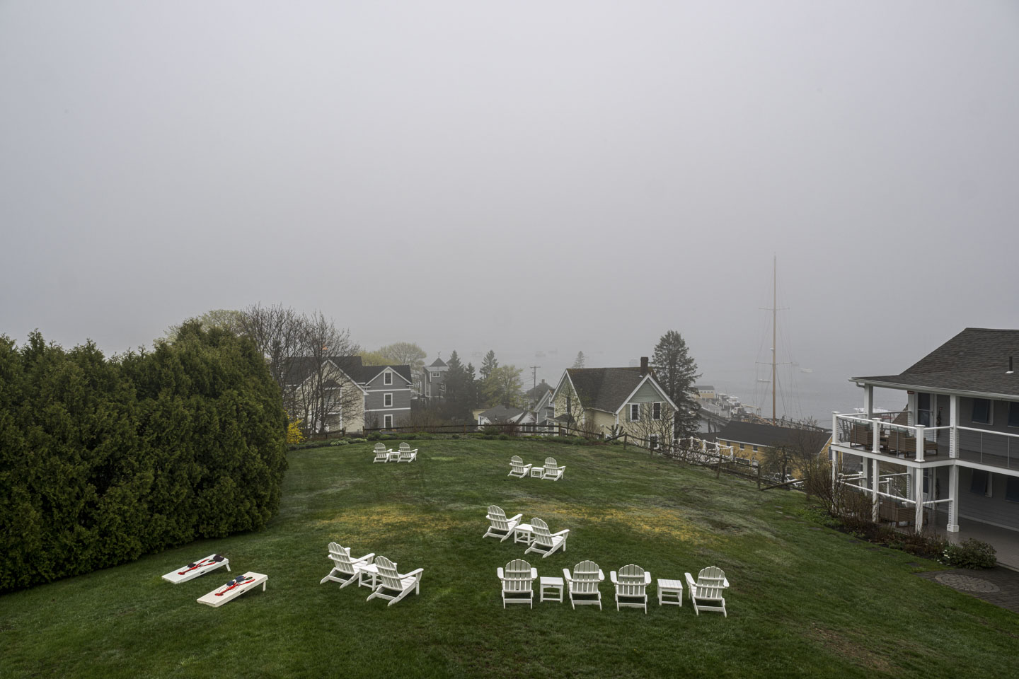 The lawn and chairs of Topside Inn and some of the Boothbay Harbor buildings can be seen but the water is hidden by fog.