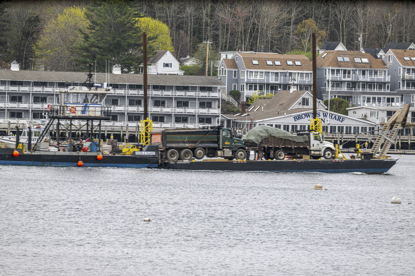 The tugboat is pushing the float that has full dump trucks.