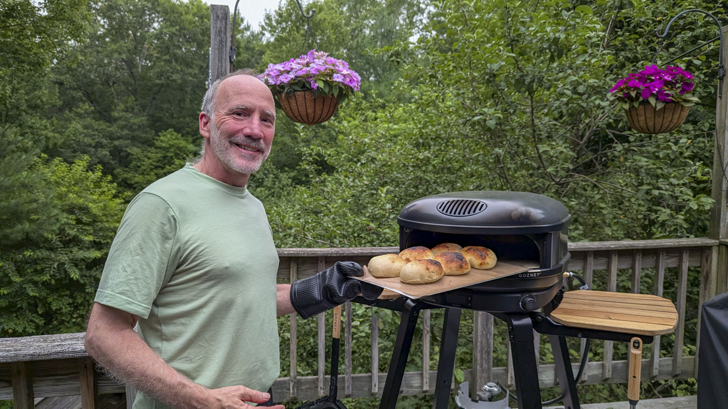 Paul is holding some rolls that he just removed from the pizza oven.