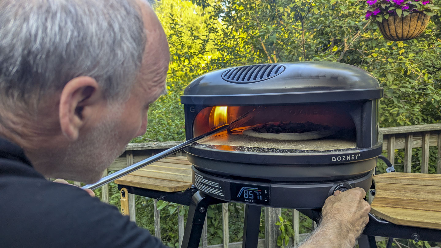 Paul is turning down the oven temperature while shielding the pizza.