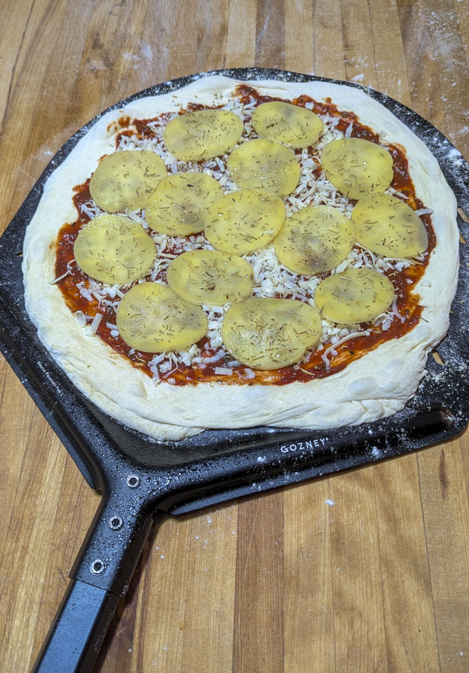 An uncooked pizza is formed and sitting on a black peel
